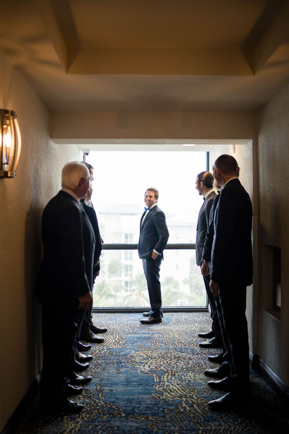 Groomsmen line up along hotel hallway window in creative silhouette wedding photograph series.