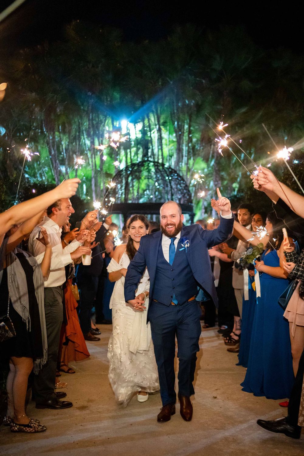 Wedding party exits through a sparkler tunnel at nighttime as guests line the pathway holding lit sparklers.