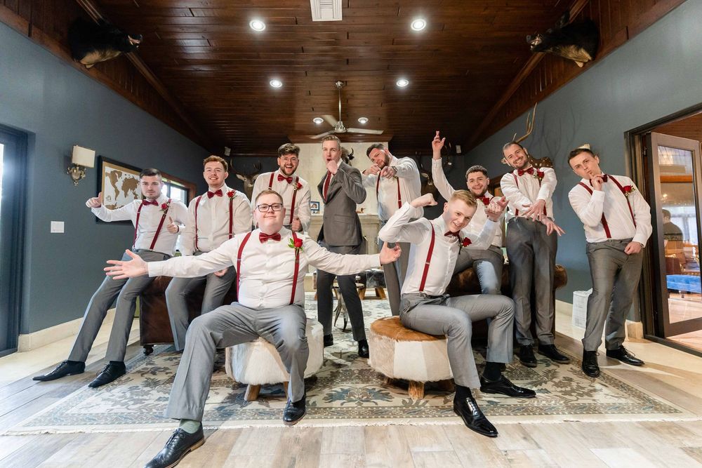 A cheerful group in matching gray suits and suspenders strike playful poses together in an indoor venue.