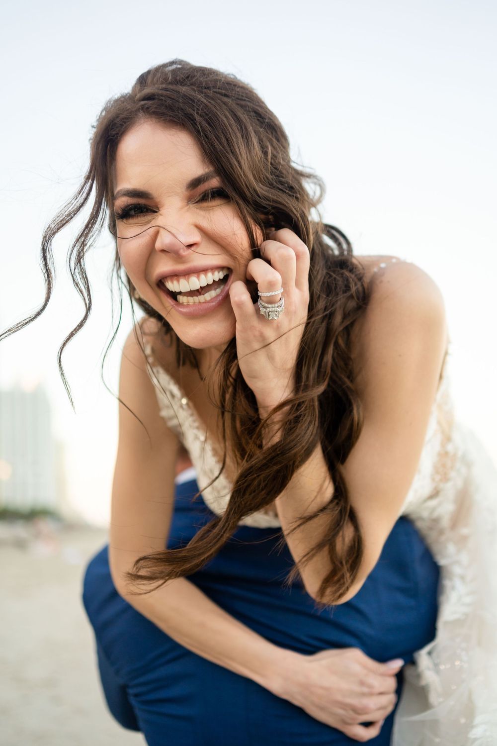 Candid portrait showing genuine laughter and joy while wearing a white dress and ring on beach during sunset.