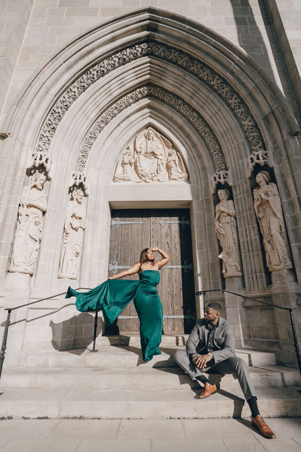 Artistic couple pose at a gothic church entrance with flowing green dress and formal attire.