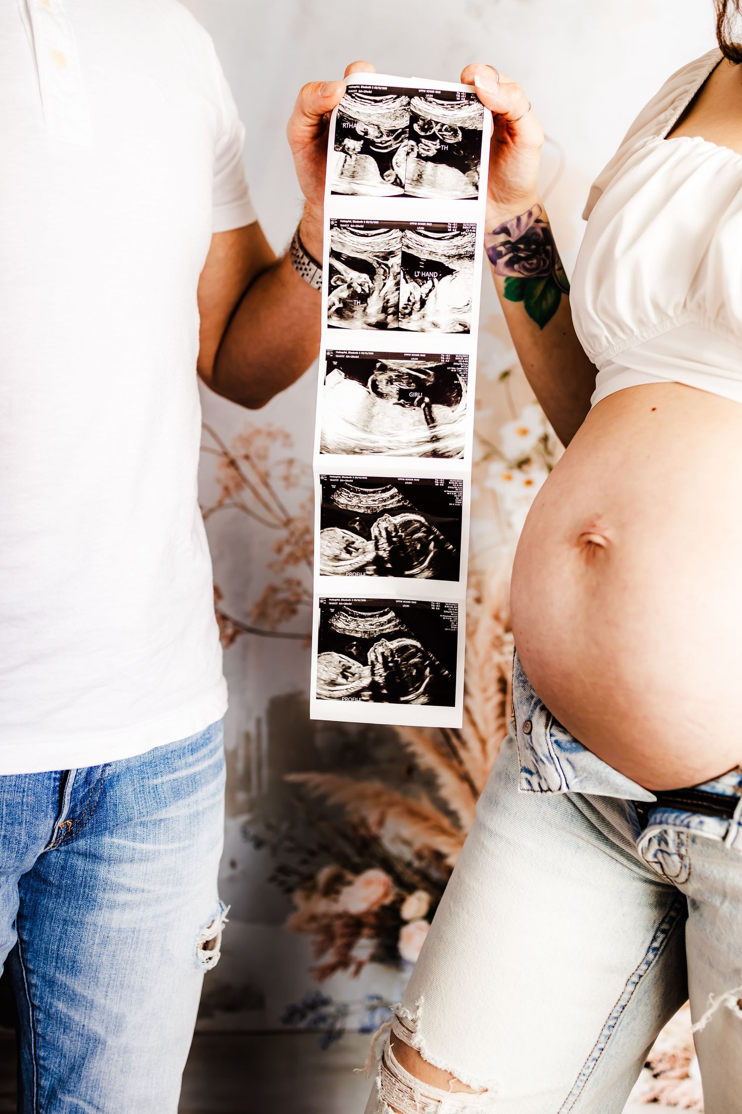 Couple holding ultrasound photos next to pregnant belly in ripped jeans, showing maternity announcement moment.