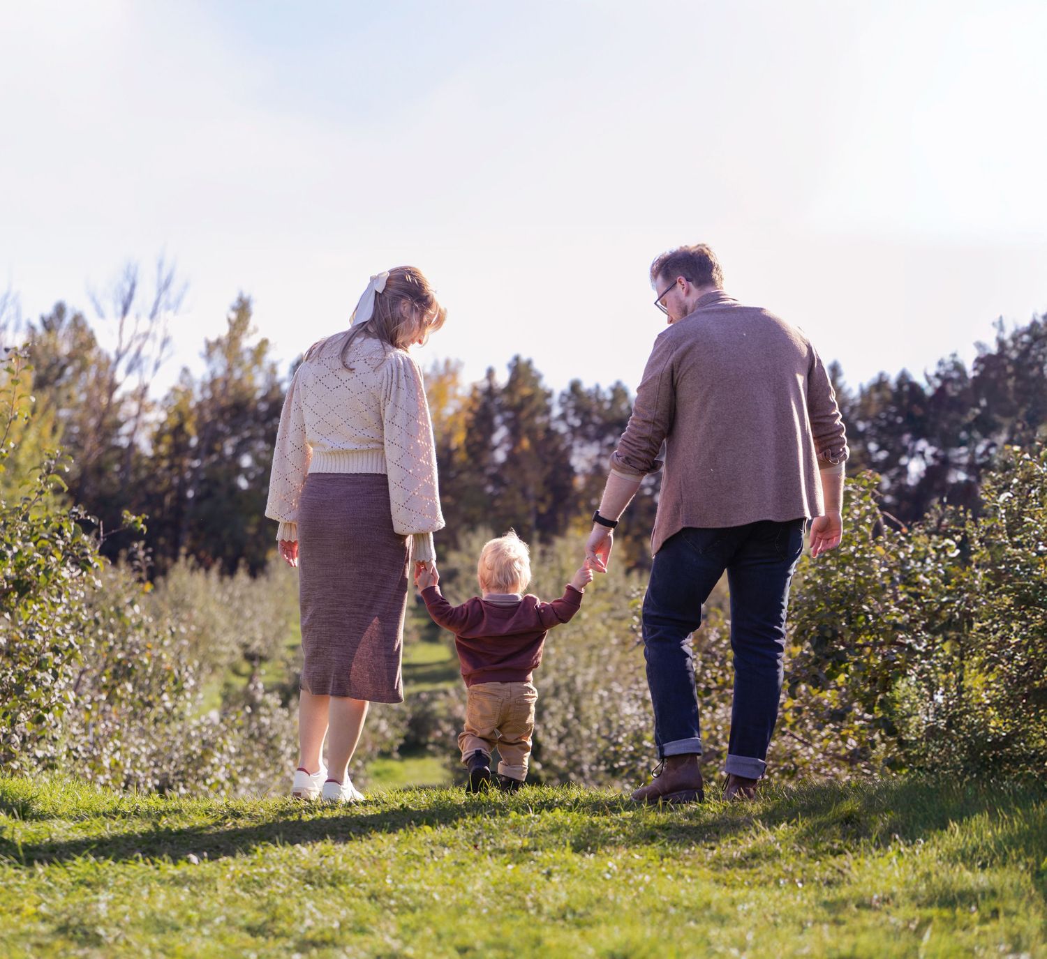 A couple and child walking together on a tree-lined path in a park.