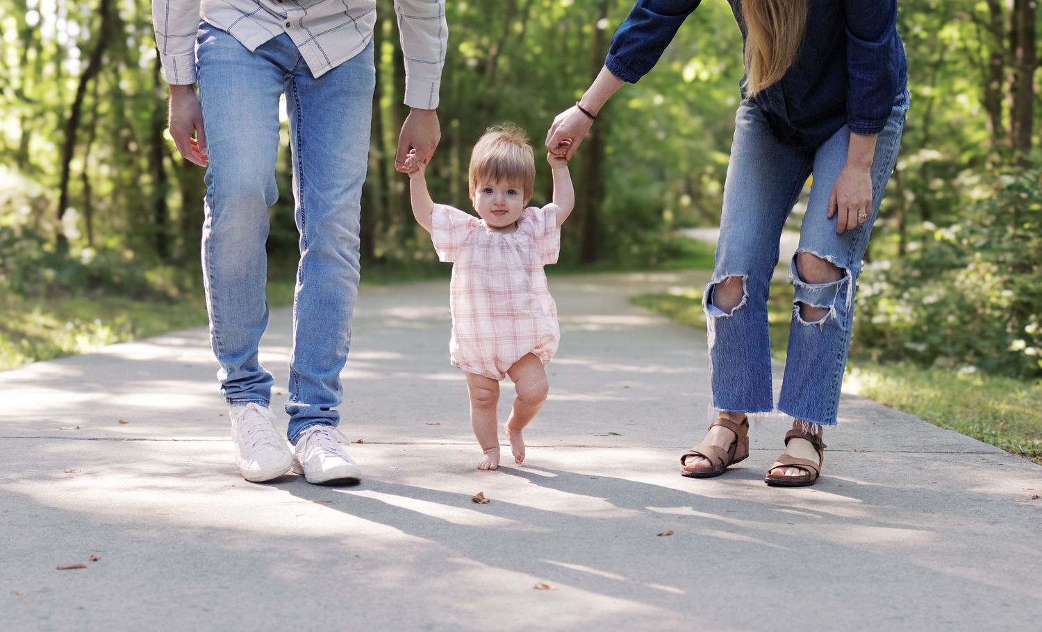 A couple and child walking together on a tree-lined path in a park.