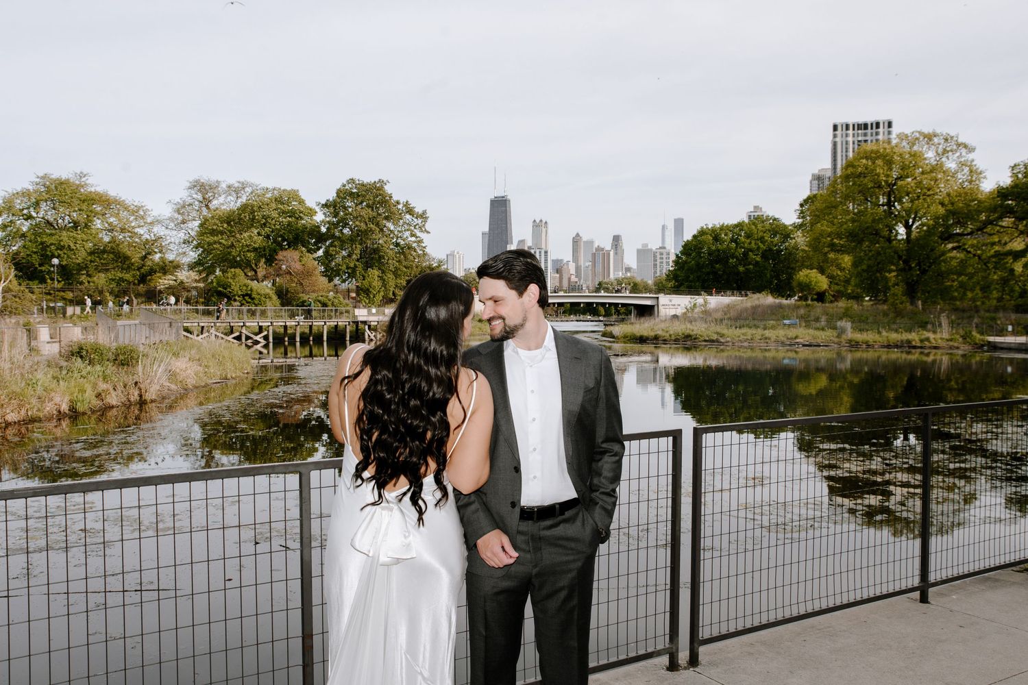 Two people embrace at Lincoln Park's Nature Boardwalk with the Chicago skyline in the background during sunset.