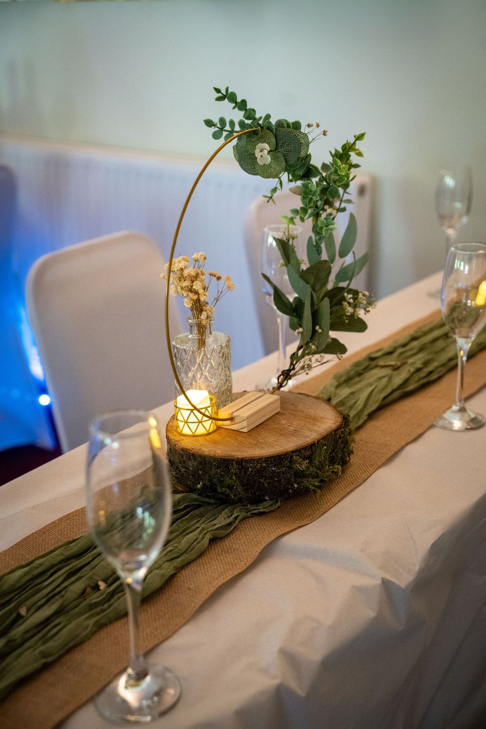 Elegant table centerpiece features wooden planks with rustic greenery and candlelit glass vessels creating romantic ambiance.