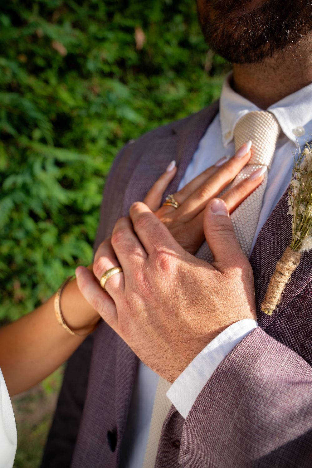 Professional close-up shot of a hand adjusting a purple tie and white dress shirt against a green leafy background.
