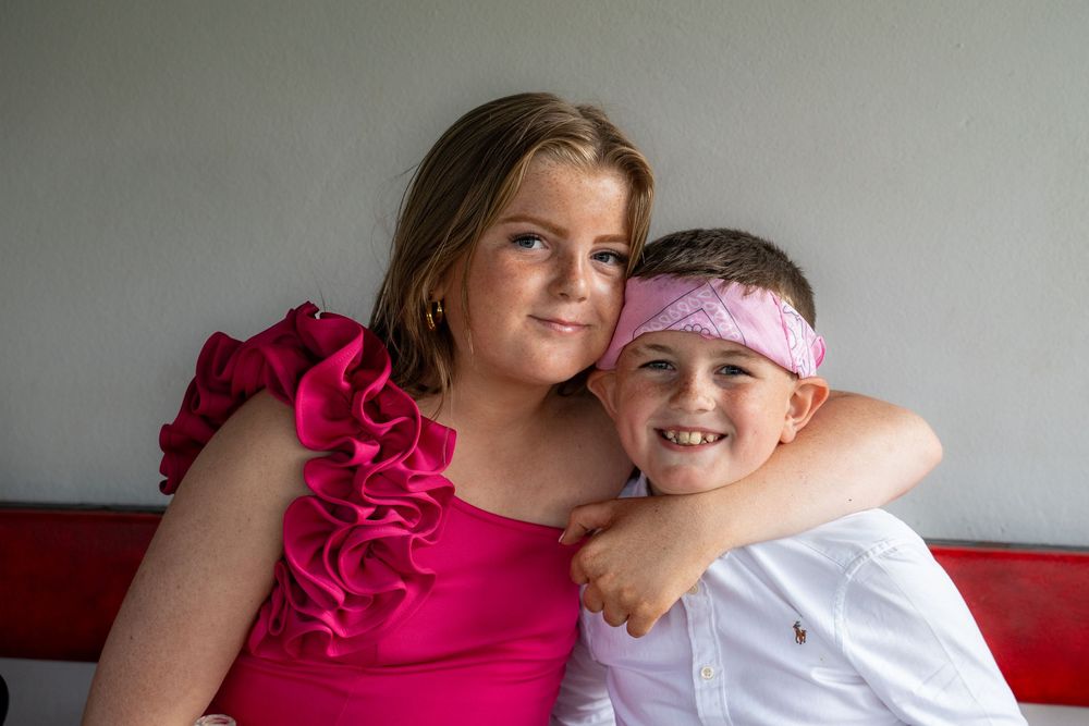 Two people smiling and embracing each other while wearing pink and white clothing in a casual setting.