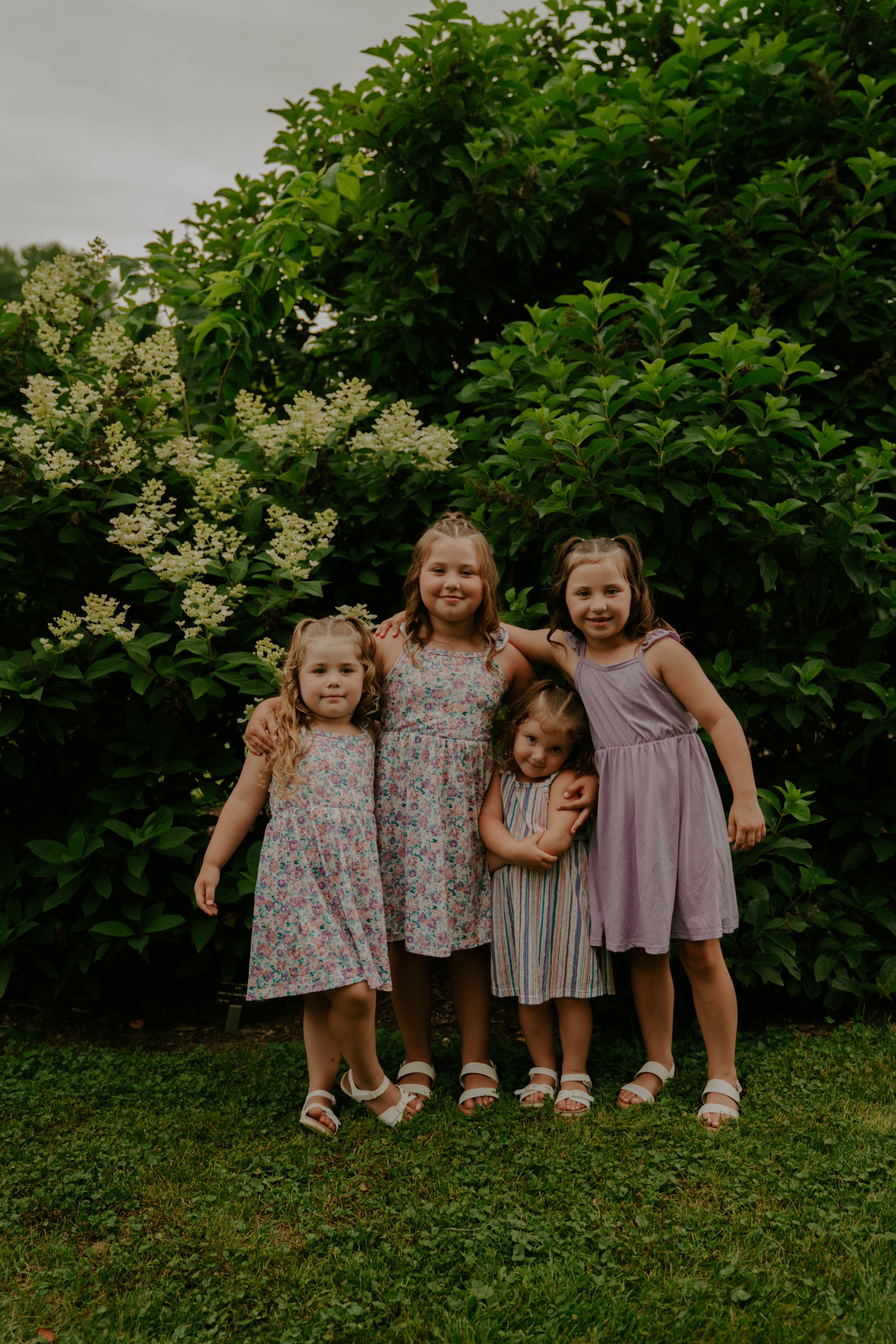 Young children sitting together on grass wearing coordinated floral and pastel dresses.