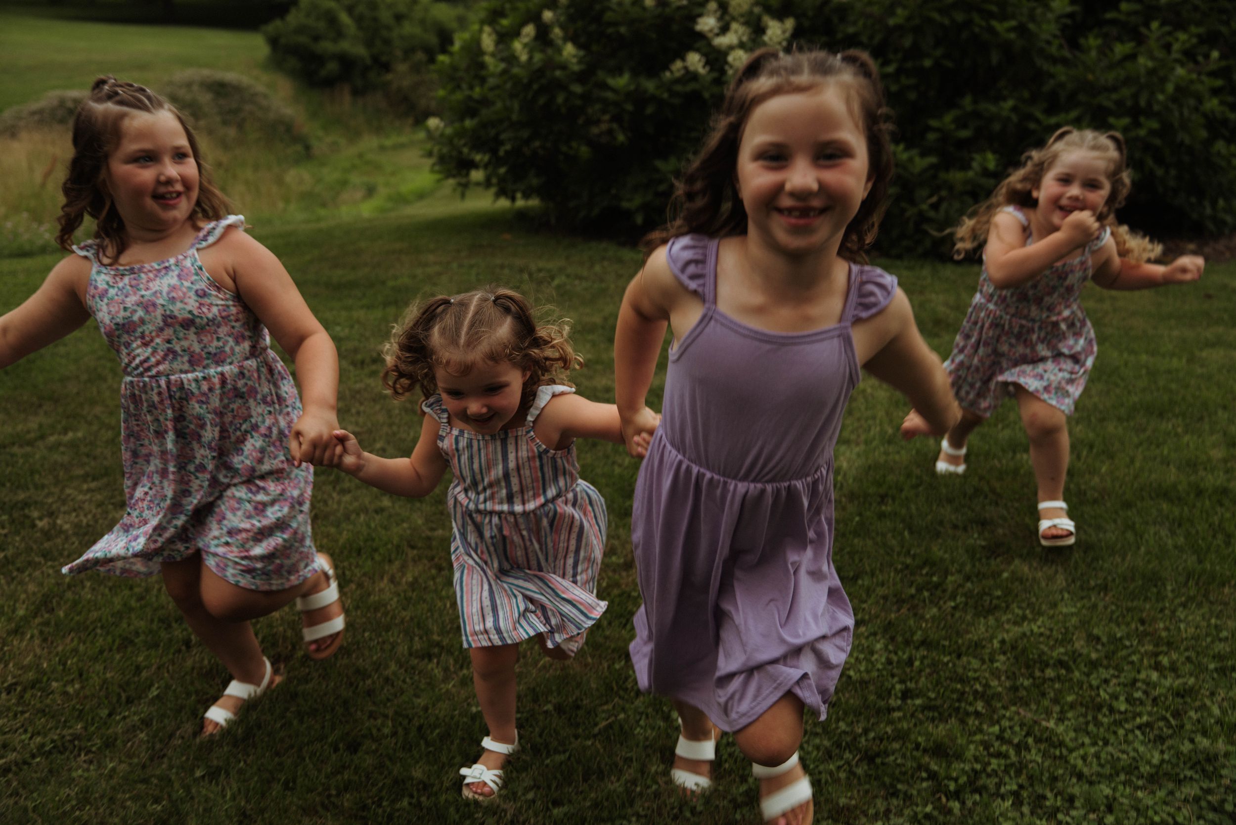 Children holding hands and playing together in a lush garden setting wearing matching dresses.