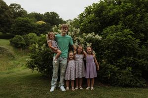 Family group portrait taken outdoors with flowering bushes and greenery in the background.