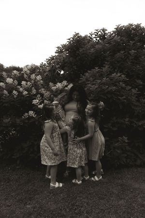 Black and white portrait of children playing together outdoors near flowering bushes.