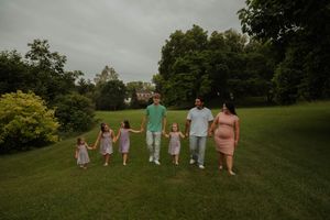 Panoramic family photo taken in green park setting under cloudy skies.