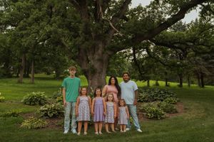 Wide landscape view of family group gathered for outdoor portrait session in park setting.