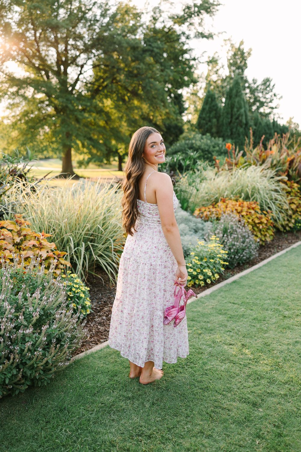 Garden scene with a floral dress against a backdrop of ornamental grasses and blooming flowers in golden evening light.