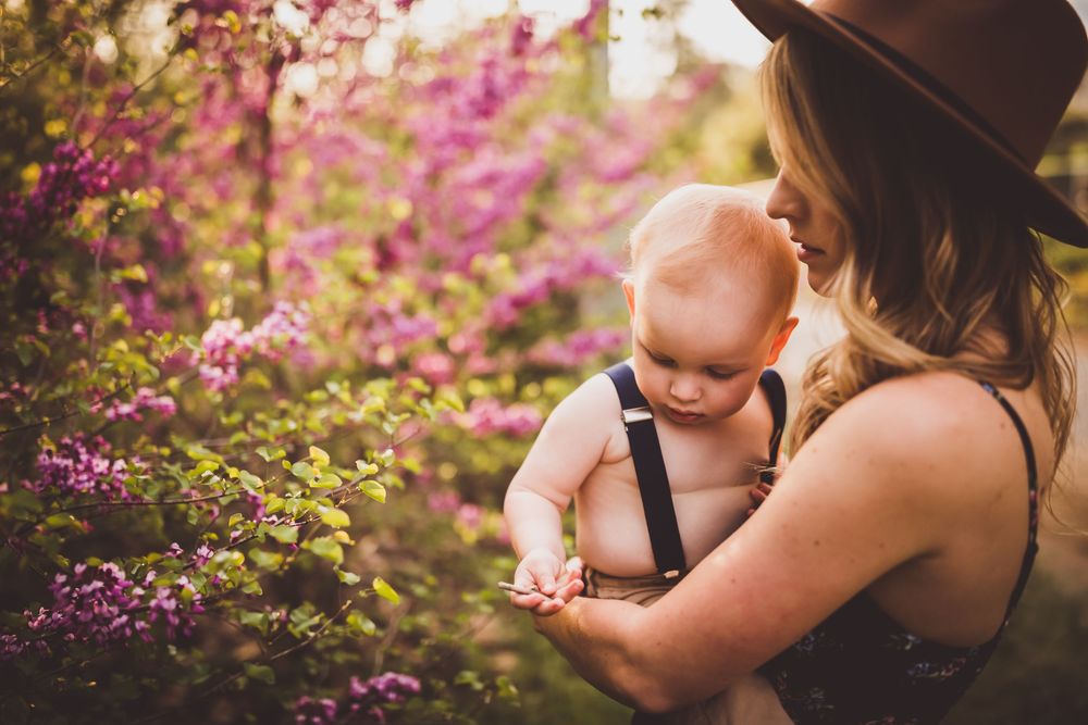 Beautiful outdoor photoshoot in a garden with pink blossoms and a brown hat at sunset.