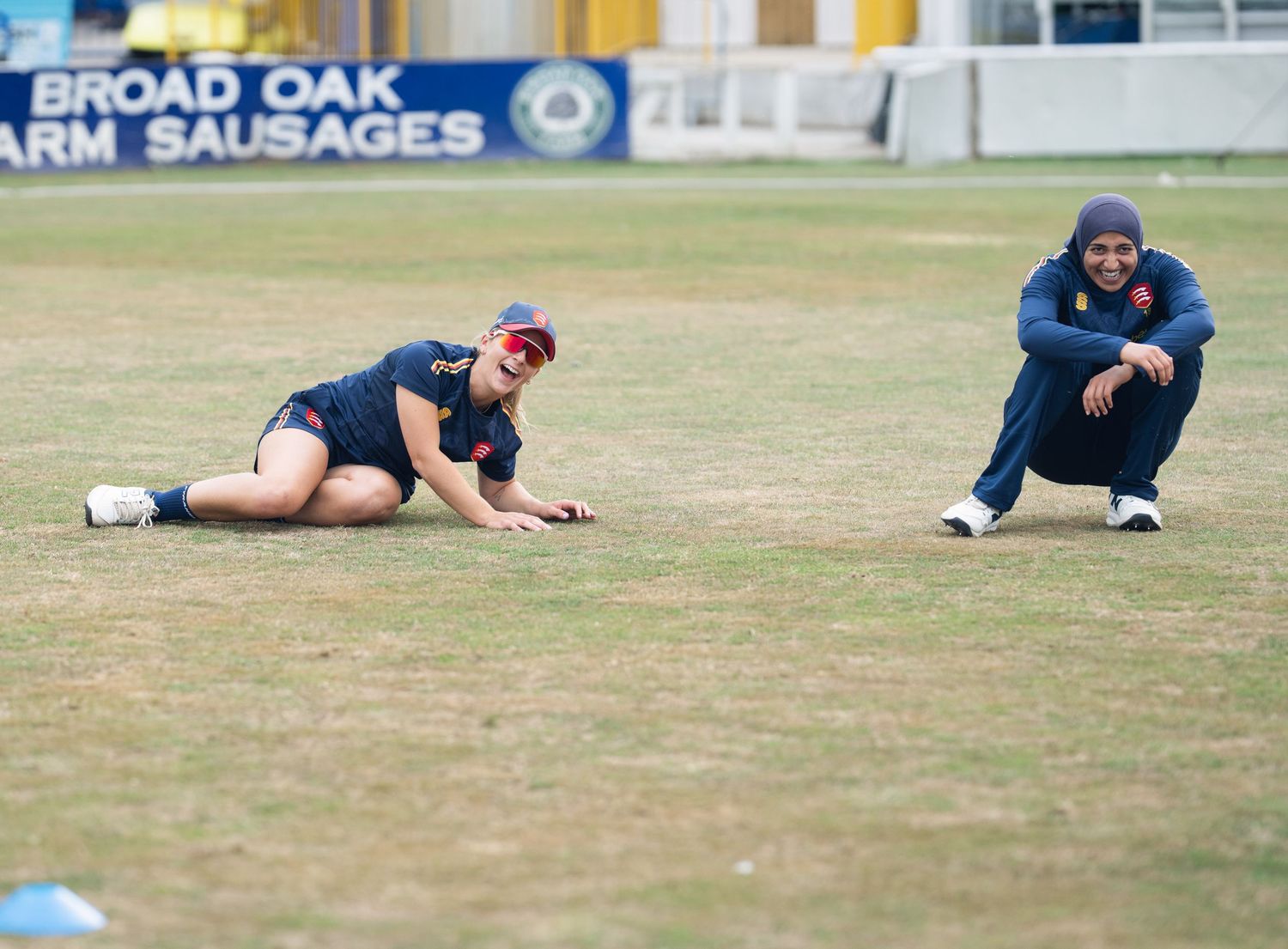 Cricket player in navy uniform and red cap runs with intense focus during bowling action on outdoor pitch.