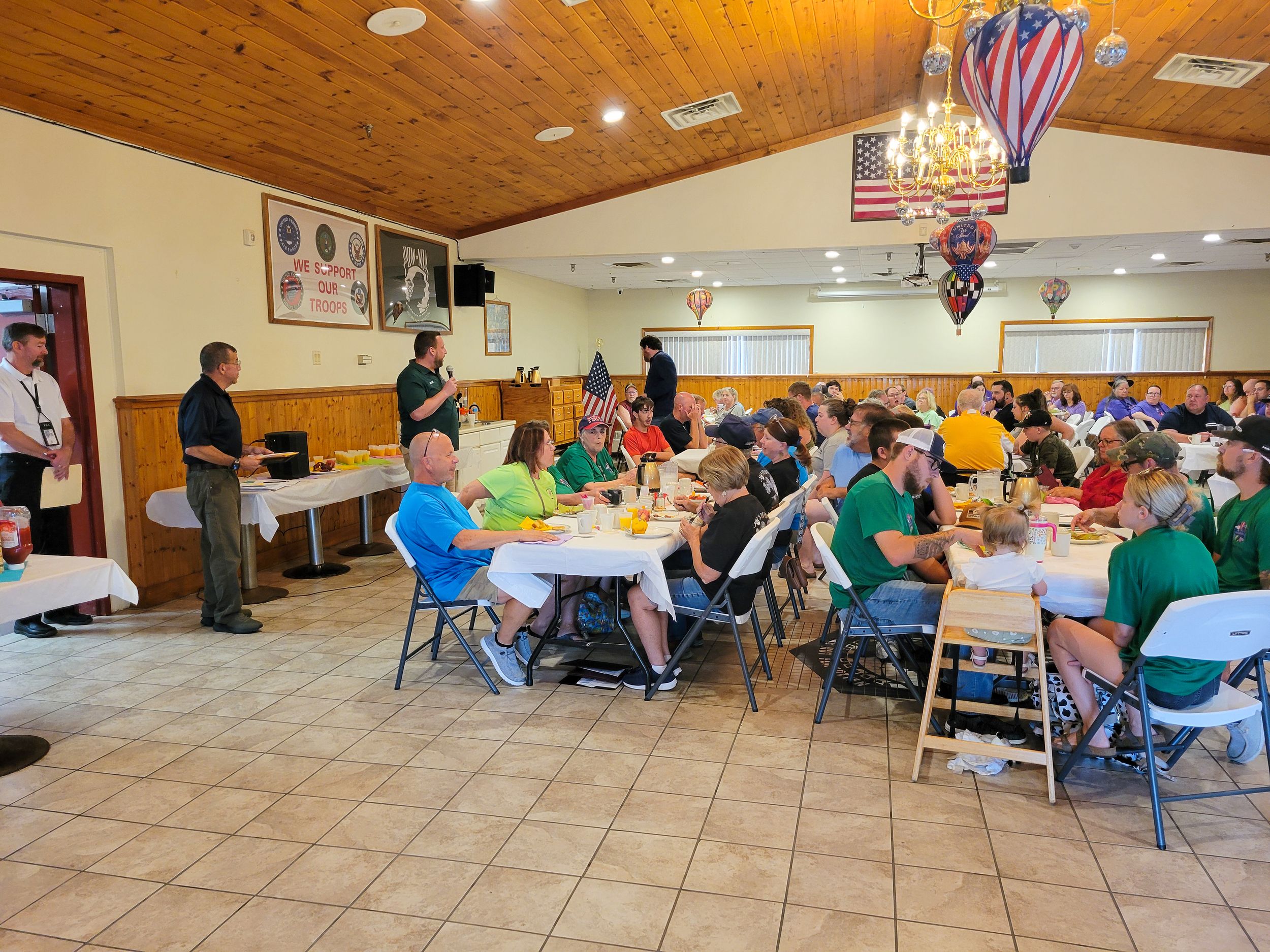 Large group dining in community hall with wooden ceiling and decorative lantern lights.