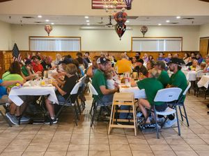 Packed dining hall with round tables and folding chairs under decorative hanging lights.