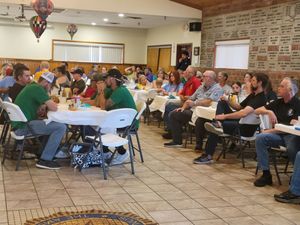 Large group seated at round tables in spacious community center during event.