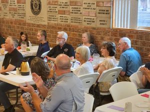 Attendees seated at round tables in brick-walled community space during event.