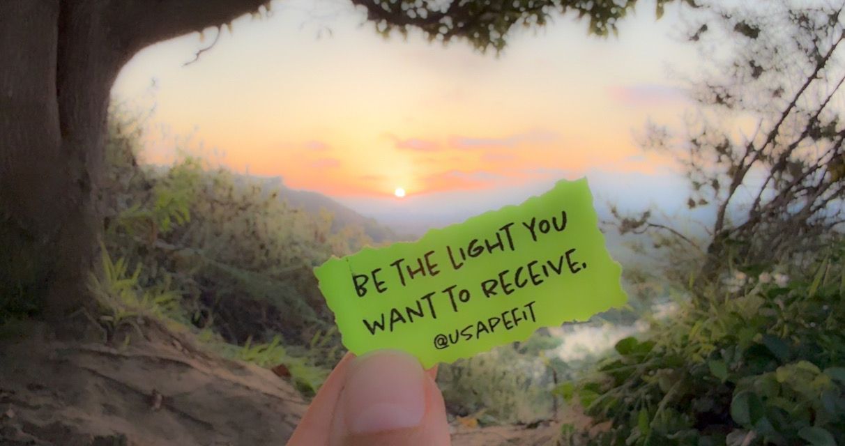 A green note held up against a sunset mountain landscape view.