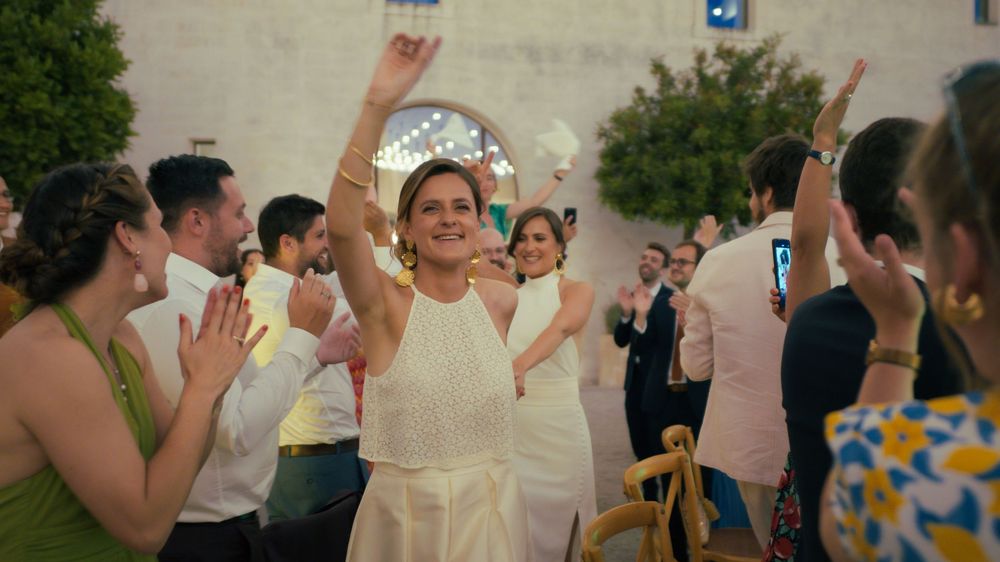 A joyful celebration occurs at a wedding reception with people dancing and raising their hands in celebration.