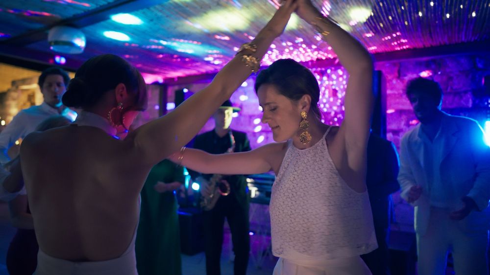 People dancing and celebrating at a vibrant party with colorful lights and glowing decorations on the ceiling.
