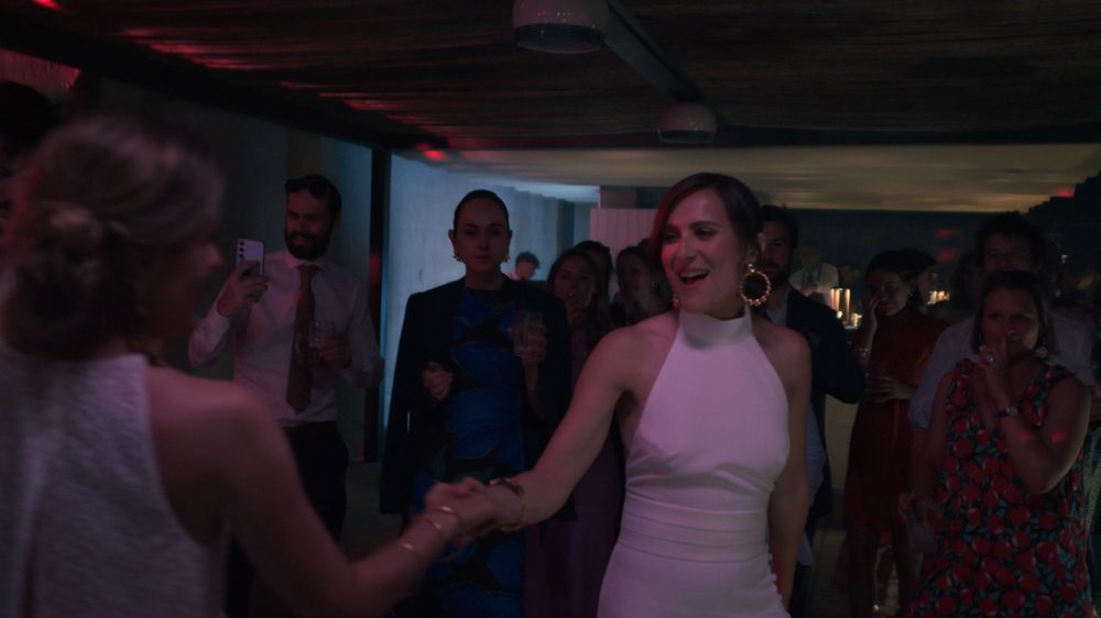 People dancing and socializing at a dimly lit party venue with pink lighting.