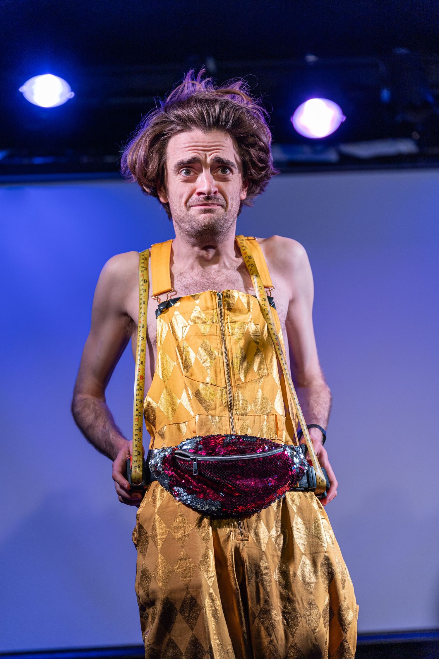 event photography Brighton a comedian stands on stage wearing a yellow jumpsuit the background is blue