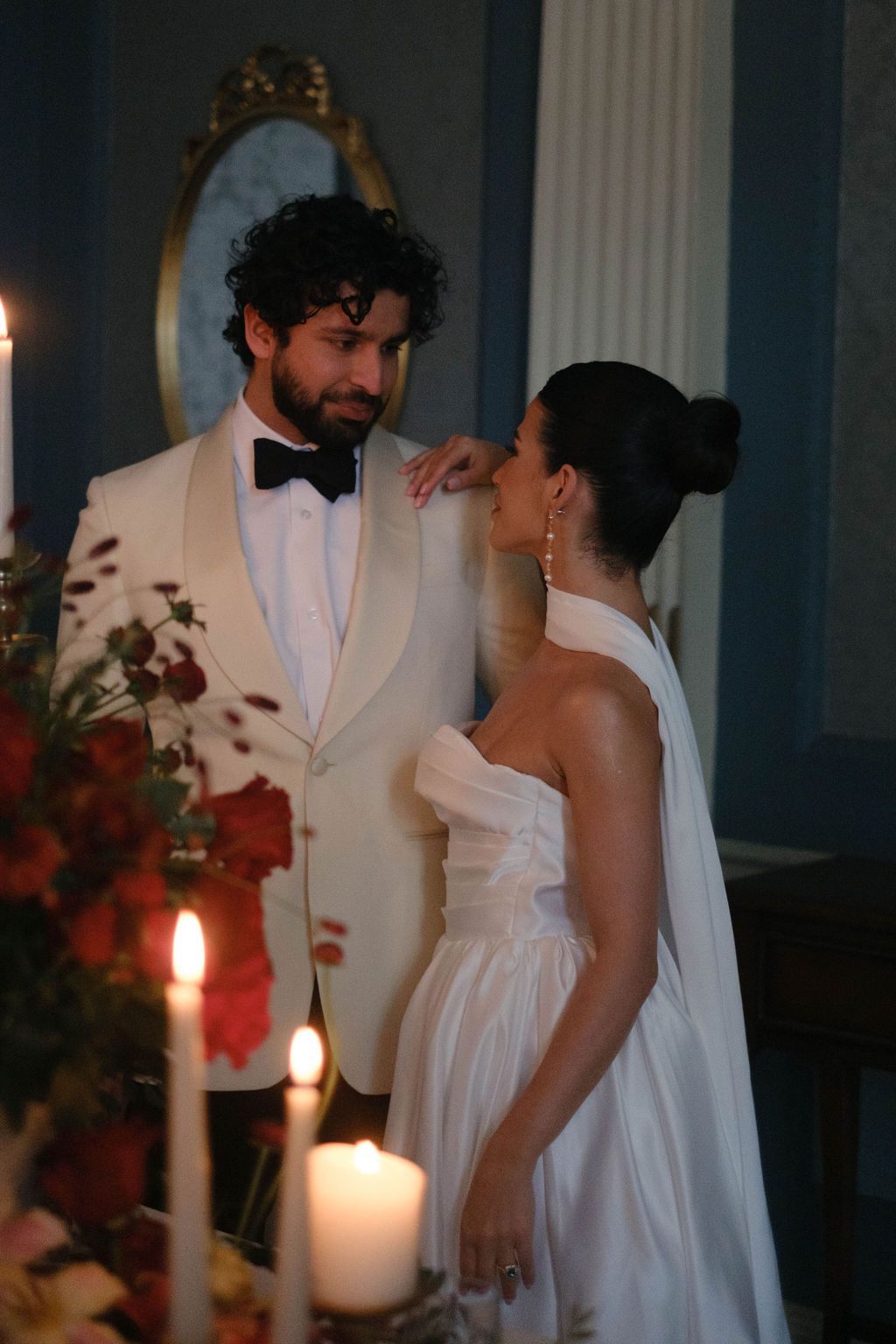 Romantic candlelit wedding reception scene with couple in white formal wear.