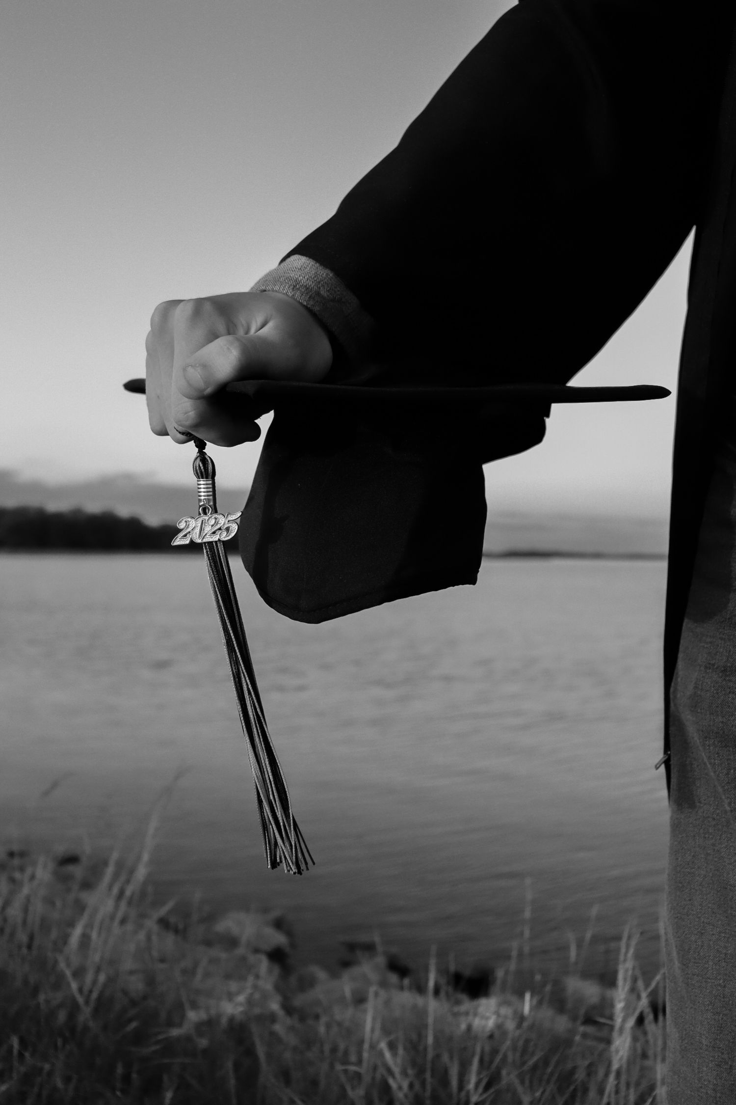 A black and white photo of hands holding a knife against a waterfront landscape at dusk.
