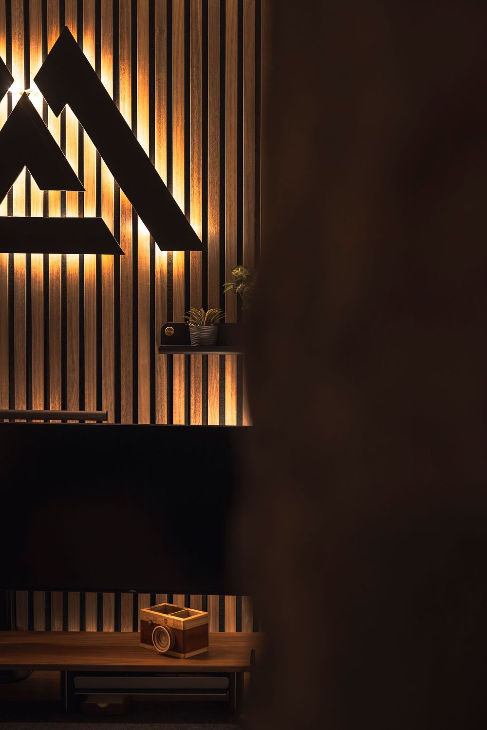 Modern interior design with illuminated triangular wall art and wooden slat accent wall creating warm ambient lighting.
