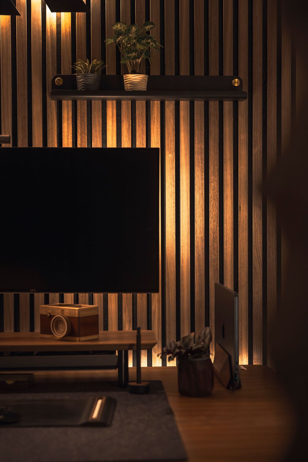 Modern living room with wood slat wall accent lighting, floating TV console, and decorative shelf with plants.