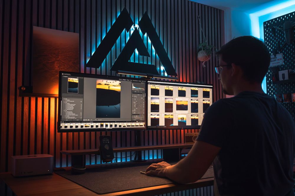 Computer editor working at a desk with glowing blue triangular light and studio monitors in a dark room.