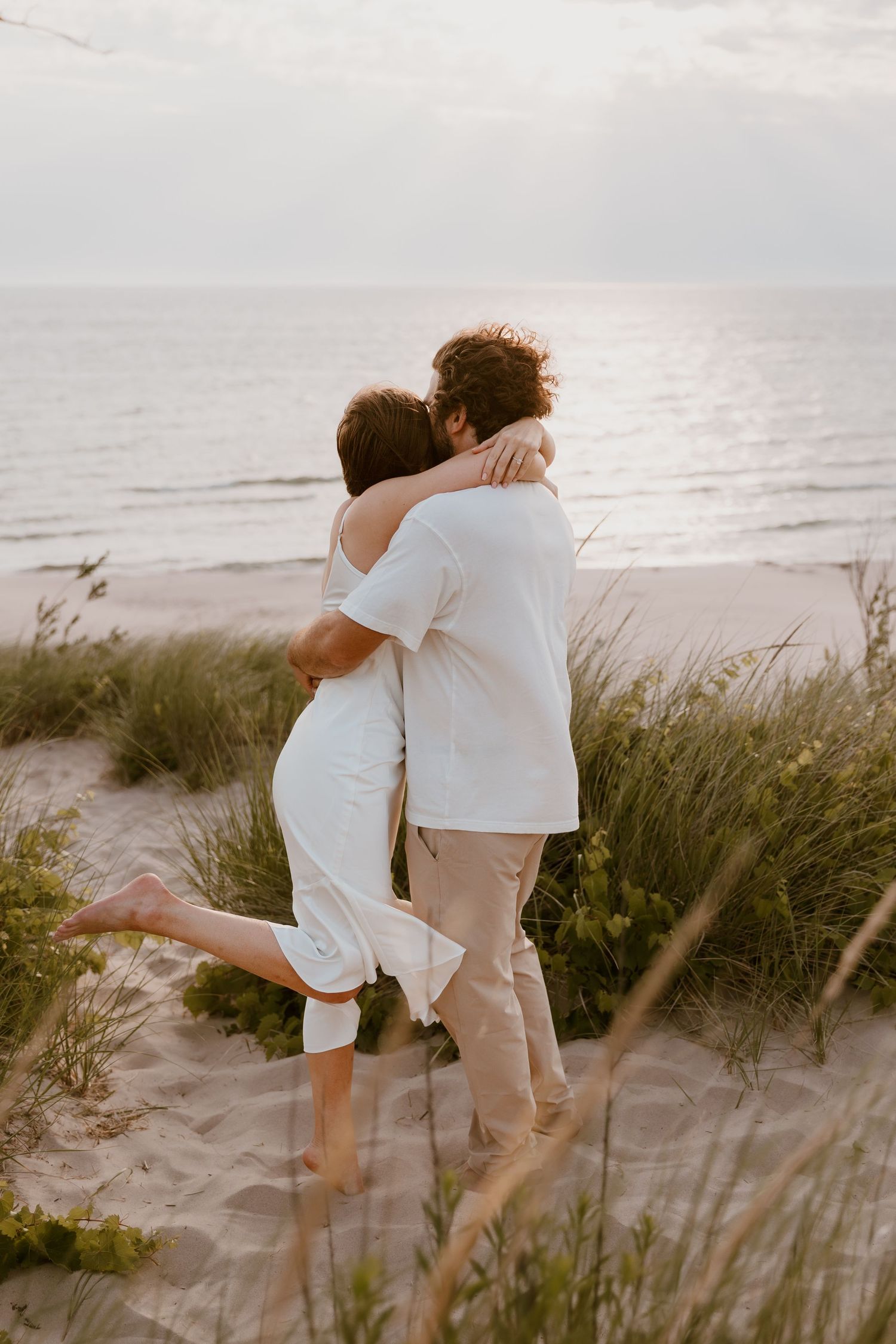 Close-up of tall beach grass swaying in the wind with soft silhouettes in the blurred background at sunset. Michigan Wedding Photographer