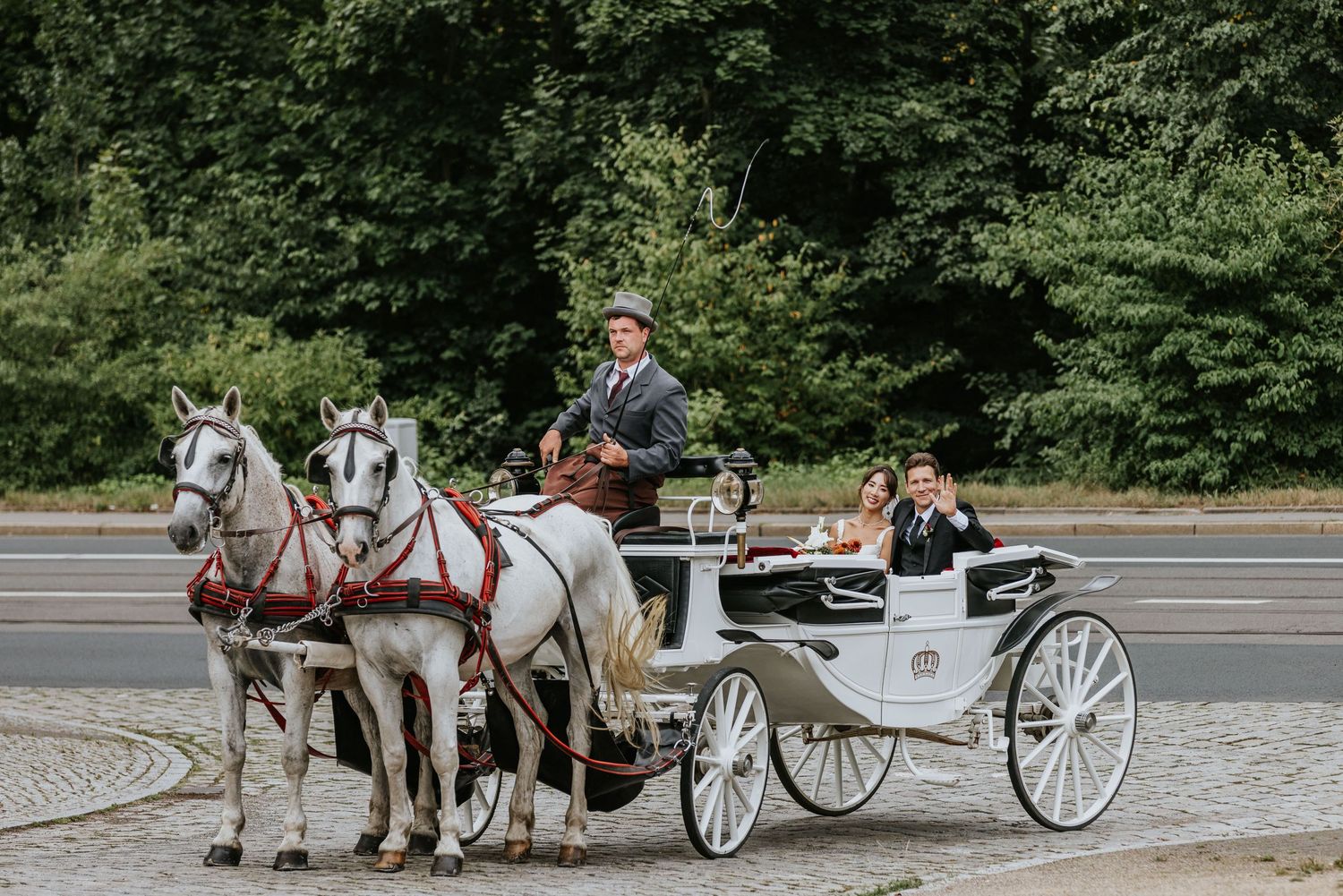 A white horse-drawn carriage waits on a cobblestone street while tourists prepare to board for a scenic ride.