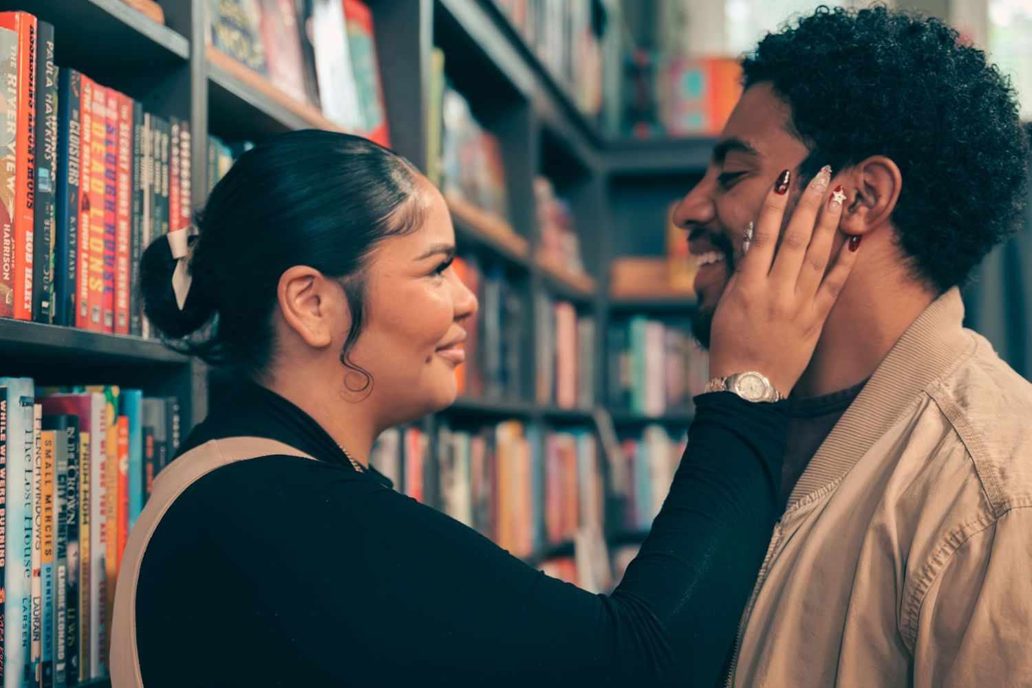 Two people looking at books together in a library while appearing to have an intimate conversation.