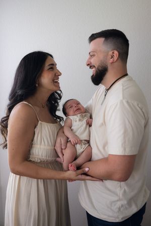 A heartwarming family portrait with a newborn baby dressed in white against a light background.