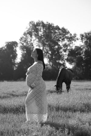 Artistic black and white portrait of a person in a lace dress standing in a field.