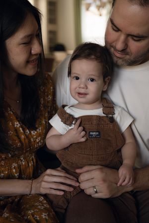 A family shares a tender moment with their baby wearing brown overalls.