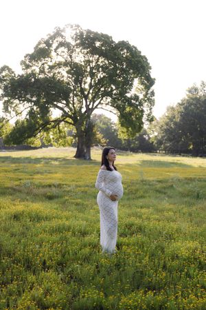 Person in white dress walks through a sunlit meadow with wildflowers and oak trees.