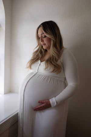 A series of intimate maternity photos showing a woman in a white dress against a neutral wall.