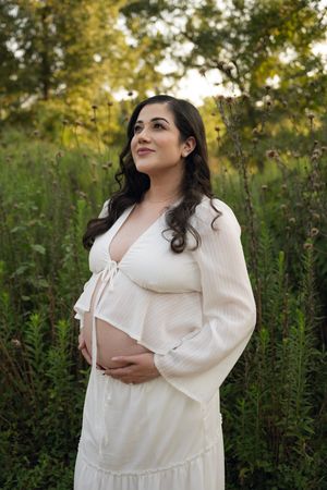 A woman in a flowing white dress poses elegantly against a lush garden backdrop.