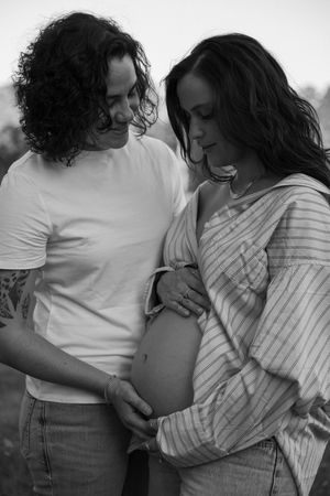 A black and white, nostalgic image of a couple cradling a baby bump during their maternity photos