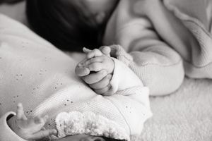 Black and white photo of a newborn baby holding a parent's finger, wrapped in a soft knit blanket.