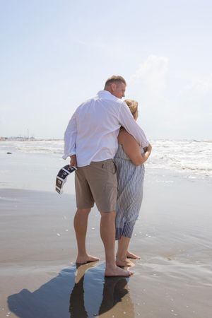 Couple wading in shallow ocean waves at the beach on a sunny day.