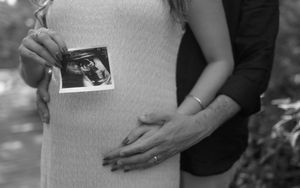 Close-up of hands holding ultrasound photo against white fabric.