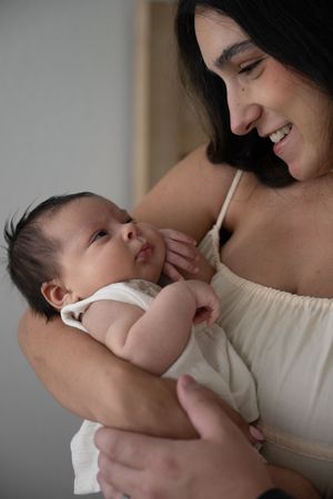 A sweet bonding moment between parent and baby dressed in white against a neutral background.