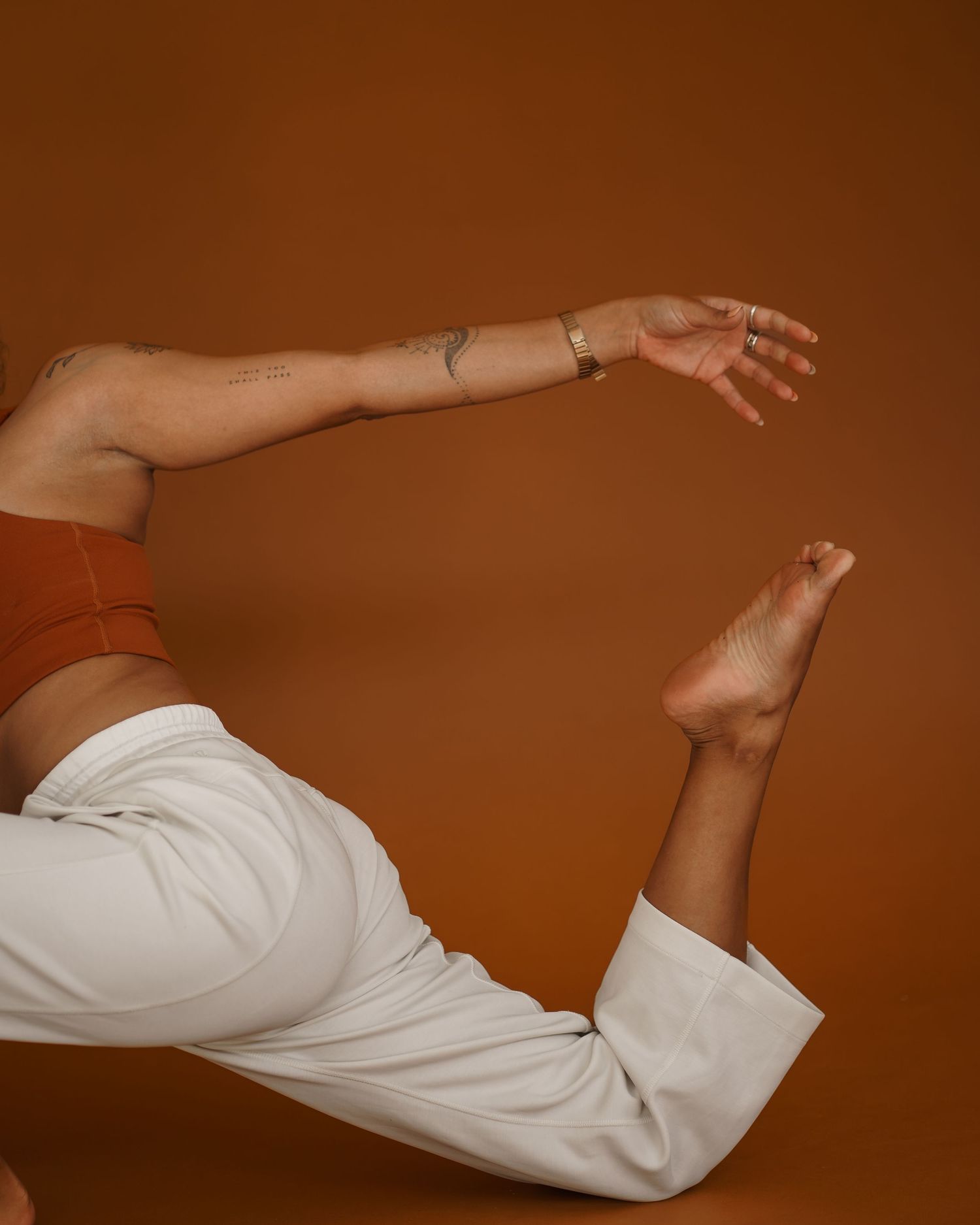 Artistic photo of an arm and leg in white pants against a warm brown background showing graceful movement and flow.